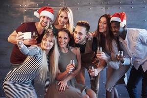 Group beautiful young people doing selfie in the new year party, best friends girls and boys together having fun, posing emotional lifestyle people. Hats santas and champagne glasses in their hands photo