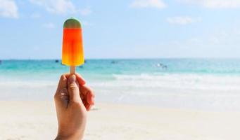 Ice cream stick in hand with sea background - Colorful ice cream fruit on beach in summer hot weather ocean landscape nature outdoor vacation photo