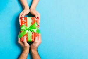 Top view of two people sharing a present on colorful background. Holiday and surprise concept. Close up photo